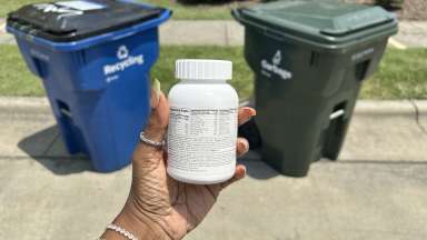 pill bottle held in front of a trash and recycling cart